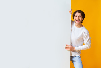 Wall Mural - Positive young man holding big white advertisement board with copy space