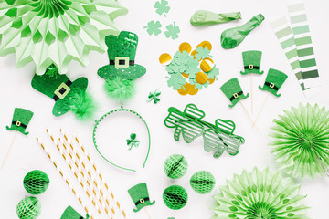 Decorations and props for St.Patrick 's Day party. Green and gold paper decorations, hair hoop with hats, clover leaf, sunglasses,  balloons, confetti and candy on white background. Flat lay, top view