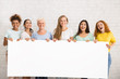 Women Holding Empty White Poster Standing Over White Wall, Mockup