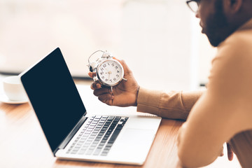 Poster - Unrecognizable afro businessman holding clock using laptop