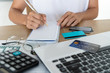 © Pattarisara - Woman writing on notebook with computer, calculator and credit card on desk, account and saving concept.