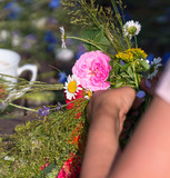 Fototapeta Lawenda - two women hands weave wreath, summer solstice tradition, wreath of field flowers, grass and cereals, wreath weaving process
