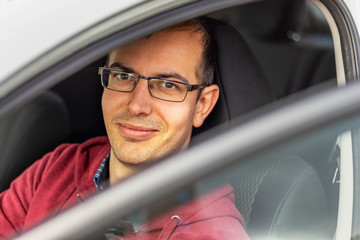 Driver with poor vision. Portrait of a man in glasses sitting at the wheel of a car and looking through the open door.