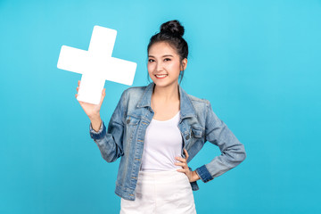 Wall Mural - Happy asian woman smiling hand on hip and showing plus or add sign on blue background. Cute asia girl smiling wearing casual jeans shirt and showing join sign for increse and more benefit concept