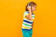 © Ivan Traimak - Little boy with curly hair in colourful t-shirt and shorts listen to music with big earphones isolated on yellow background