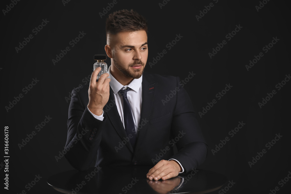 Handsome young man with bottle of perfume on dark background