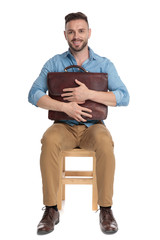 Wall Mural - happy casual man holding suitcase to chest and smiling