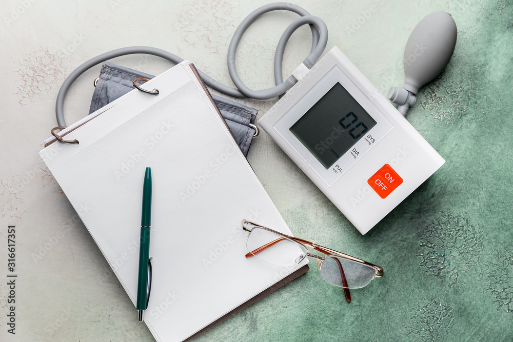 Notebook and sphygmomanometer on color background