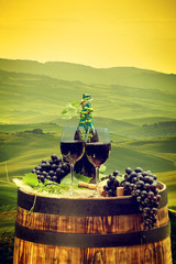 Red wine bottle and wine glass on wodden barrel. Beautiful Tuscany background