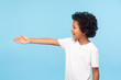 © khosrork - Profile of polite cheerful preschool boy with curly hair in white T-shirt giving hand to handshake, gullible trusting child meeting with friendly smile. indoor studio shot isolated on blue background