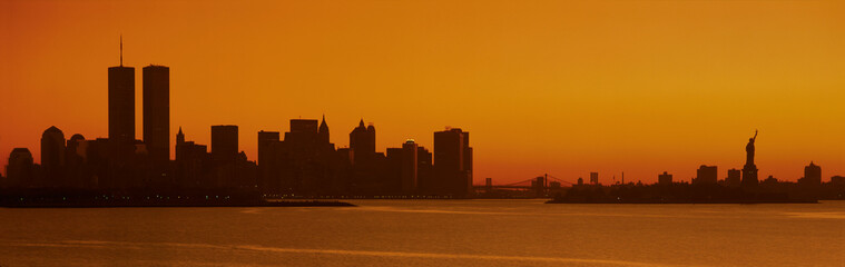 Fototapete - This is the Manhattan skyline from New Jersey. It shows the Statue of Liberty on the right, the world Trade Towers on the left and the skyline in silhouette at sunrise.
