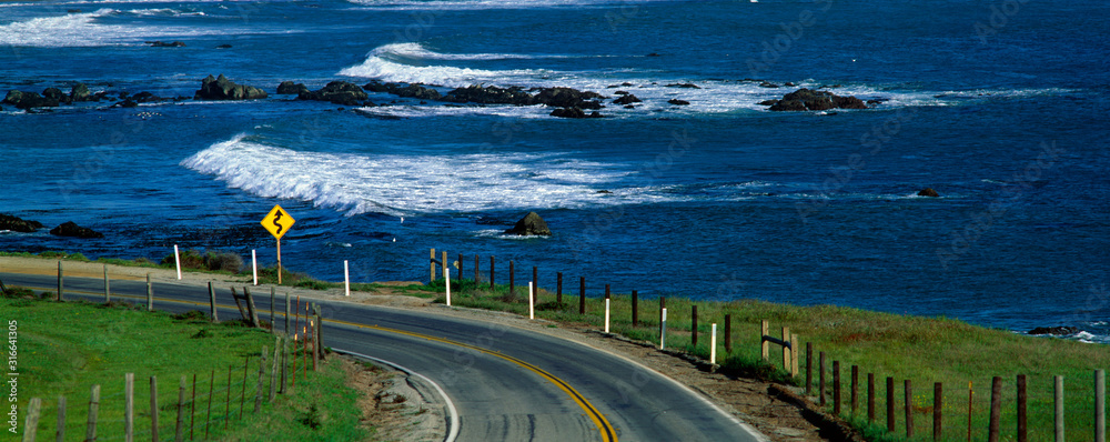 This is Route 1, also known as the Pacific Coast Highway. The ocean is to the right of the road which curves around a bend. - obrazy, fototapety, plakaty 