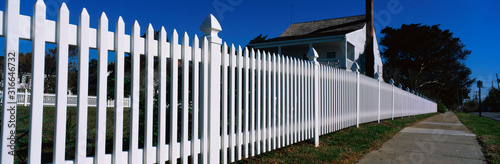 Fotografía This is a close up of a white picket fence and a typical looking suburban house