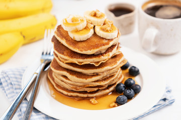 Pancakes with banana and golden maple syrup on white plate closeup view. Sweet breakfast, stack of fluffy buttermilk pancakes