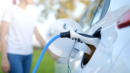 Electric car or ev is charging at station . man use the white power cable and plug on nature background. eco and clean energy concept with the mobile phone smart technology. zero gas no transmission