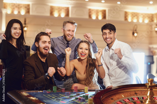 Cheerful group of friends enjoys winning poker roulette in a casino Tableau sur Toile