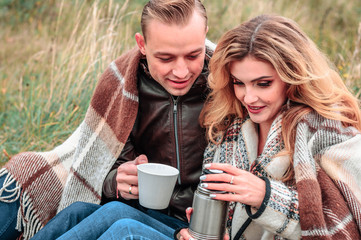 Wall Mural - young couple in love drink tea from a thermos outdoors on a cold autumn day, concept of romantic love relationships