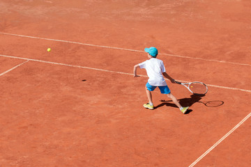 Boy on the tennis court. A child tennis player tries to hit forehand correctly. Active game for the development of children. Sports concept. Space for text.