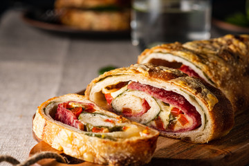 Traditional Italian Stromboli stuffed with cheese, salami, red pepper and spinach. Photo in a dark style.