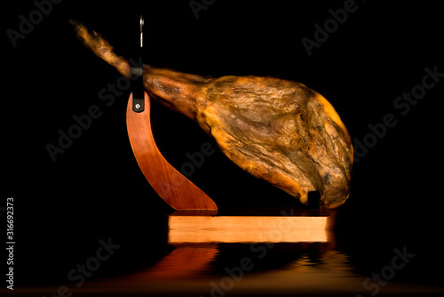Fotomural Whole Iberian ham leg in a ham holder reflected on black