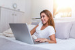 © Graphicroyalty - Happy casual beautiful woman working on a laptop laying on the bed in the house. Freelancer woman working on her laptop at home