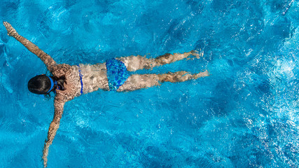 Wall Mural - Active girl in swimming pool aerial drone view from above, young woman swims in blue water, tropical vacation, holiday on resort concept