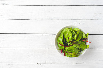 Wall Mural - Green mixed salad with spinach, arugula and beetroot leaves in bowl on white wooden table with copyspace. Top view