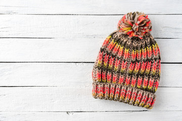 Wall Mural - Overhead shot of colourful winter hat with pompon on white wooden background with copyspace