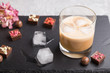 Sweet chocolate liqueur with ice in glass on a gray concrete background and black stone slate board. Side view, selective focus.
