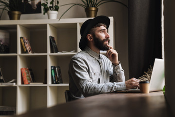 Photo of thinking young man typing on laptop and drinking coffee