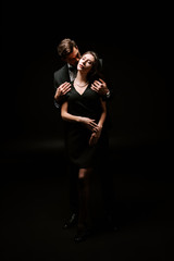 Wall Mural - man standing and kissing beautiful woman in dress on black