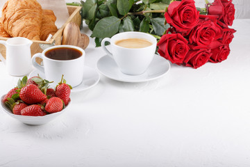 Two cups of coffee, strawberry and croissants on white table.  Festive breakfast with a bouquet of red roses. Happy Valentines day. Copy space.