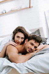 Wall Mural - happy young woman lying on bed with muscular boyfriend