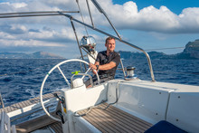 Sailor At The Helm Of Modern Sailing Yacht. Mediterranean Sea, Near Ischia Island And Capri Island On The Background, Italy.