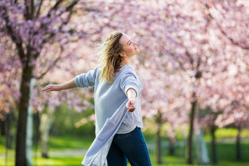 Young woman enjoying the nature in spring. Dancing, running and whirling in beautiful park with cherry trees in bloom. Happiness concept