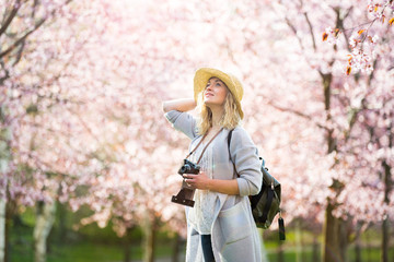 portrait of a beautiful woman in straw hat traveling in beautiful park with cherry trees in bloom, t