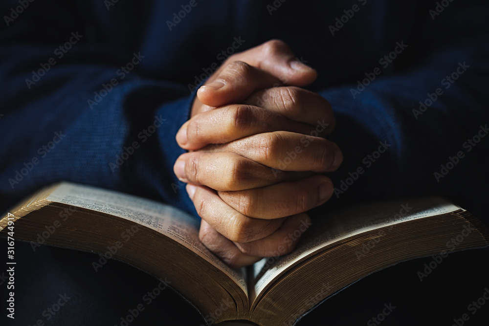 Hands folded in prayer on a Holy Bible in church concept for faith - obrazy, fototapety, plakaty 