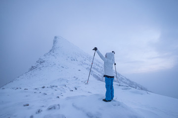 Wall Mural - man climber with trekking poles standing on snow mountain peak in gloomy