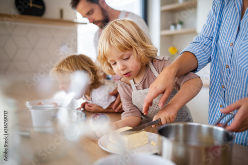Fotografía Young family with two small children indoors in kitchen, preparing food