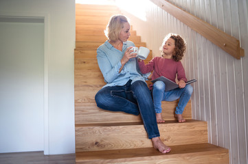 Wall Mural - A cute small girl with mother indoors at home, sitting on staircase.