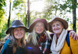Senior women friends walking outdoors in forest, looking at camera.