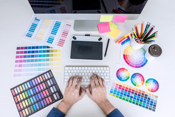 Poster - Male creative graphic designer working on color selection and color swatches, drawing on graphics tablet at workplace with work tools and accessories, top view workspace