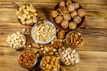 Sticker - Assortment of nuts on wooden table. Almond, hazelnut, pistachio, peanut, walnut and cashew in small bowls. Top view. Healthy eating concept