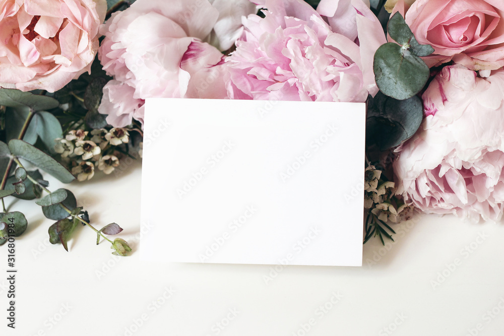 Wedding, birthday stationery mock-up scene. Blank greeting card, invitation. Decorative floral composition. Closeup of pink roses petals, peonies, hydrangea flowers, eucalyptus on white table. - obrazy, fototapety, plakaty 
