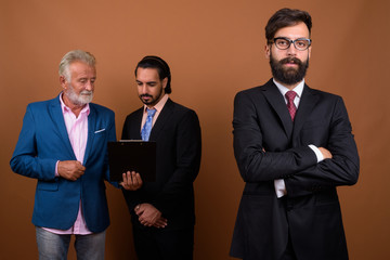 Wall Mural - Three multi ethnic bearded businessmen together against brown background