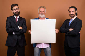 Wall Mural - Three multi ethnic bearded businessmen together against brown background