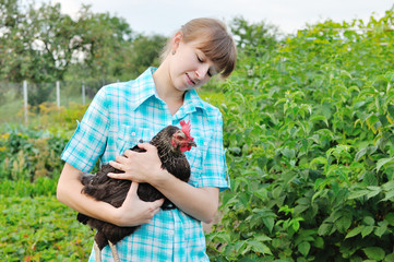 young, beautiful girl farmer with a chicken in her hands above green farm