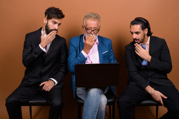 Wall Mural - Three multi ethnic bearded businessmen together against brown background