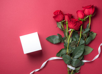 delicate bouquet of red roses lies on a red background with white pure box present. Valentines day