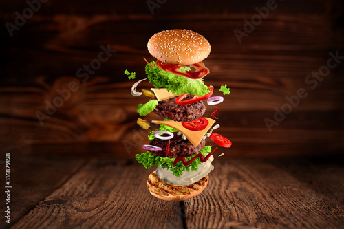 Fotomural Maxi hamburger, double cheeseburger with flying ingredients isolated on wooden background